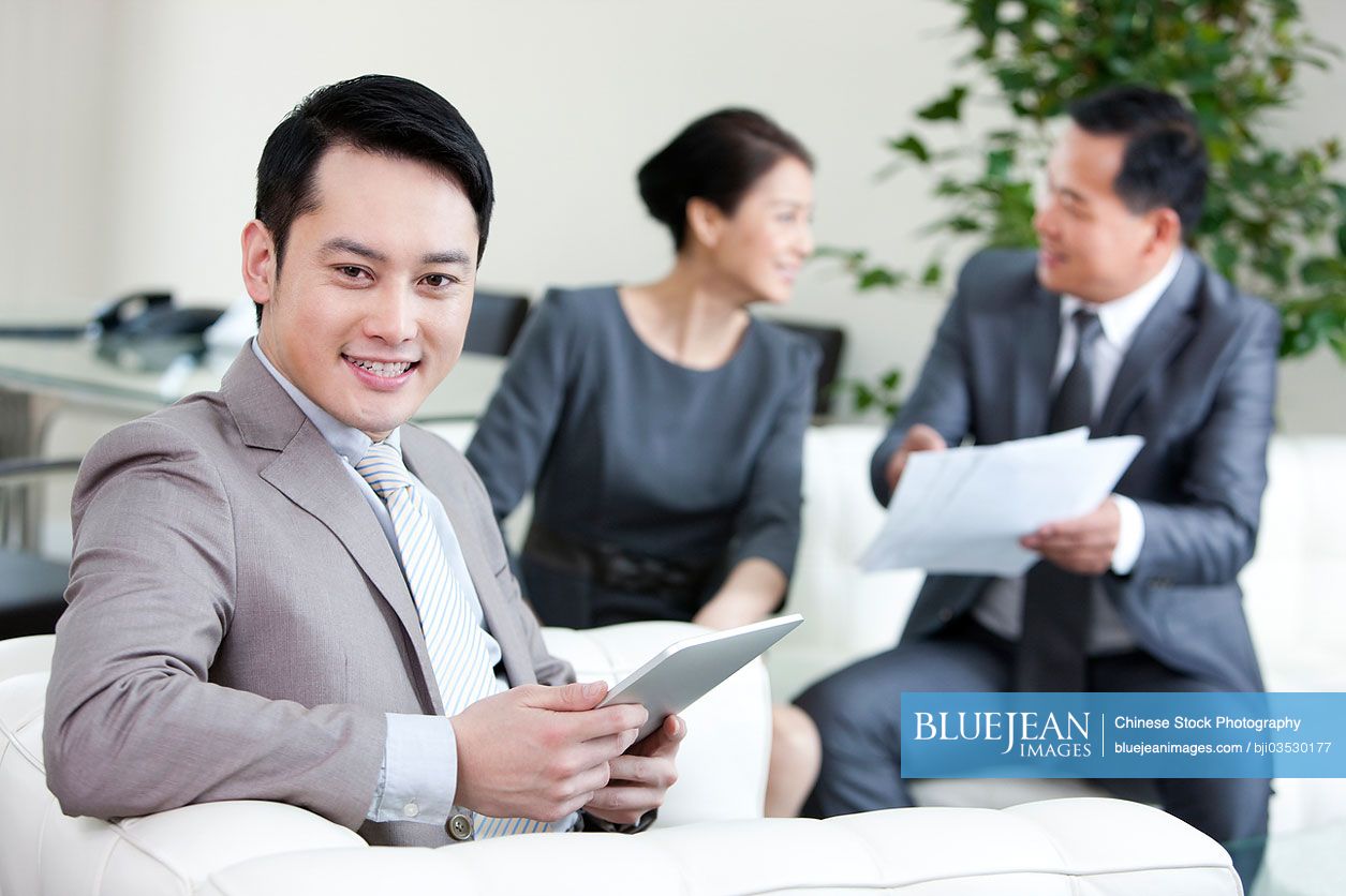 Chinese businessman holding digital tablet and partners in background