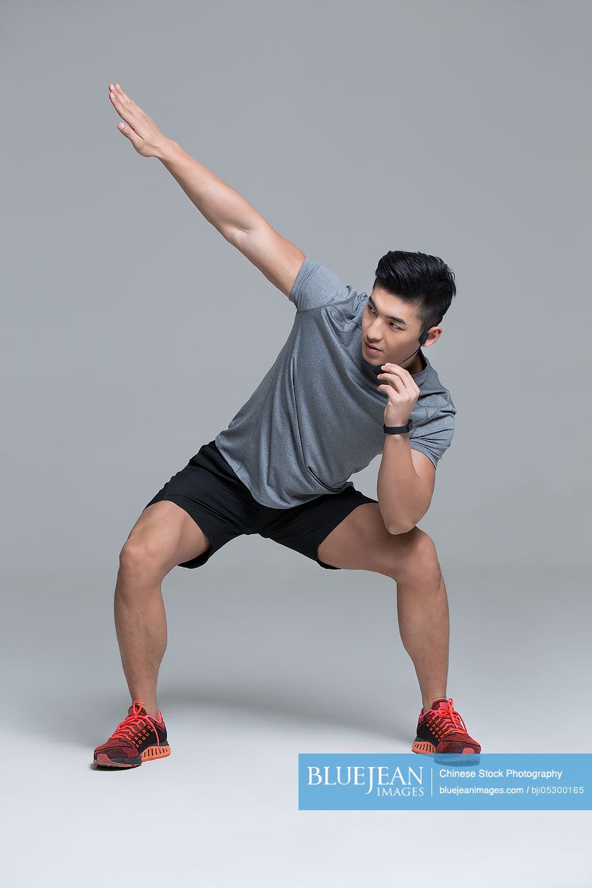 Young Chinese male trainer with headset teaching at gym