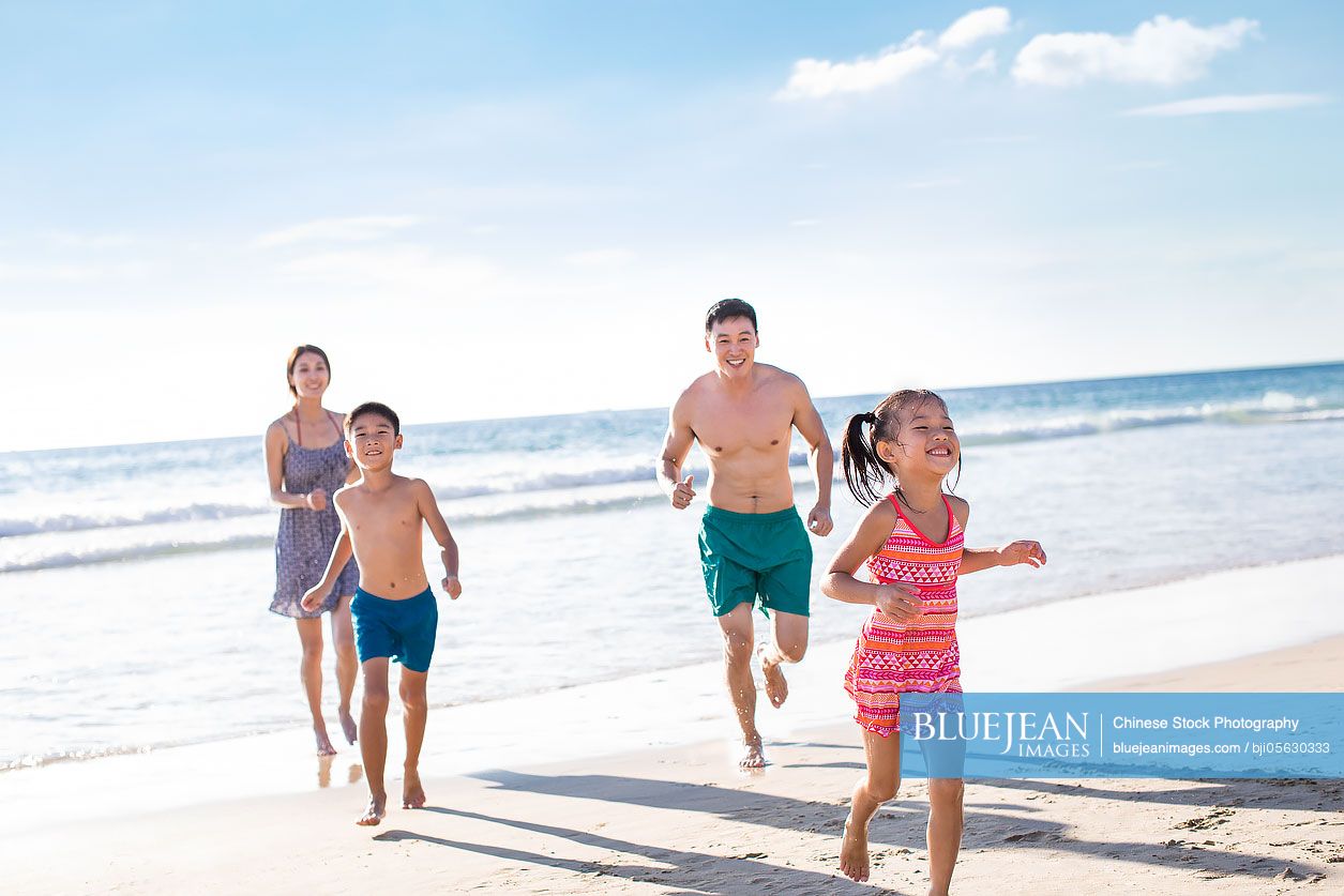 Happy young Chinese family running on beach