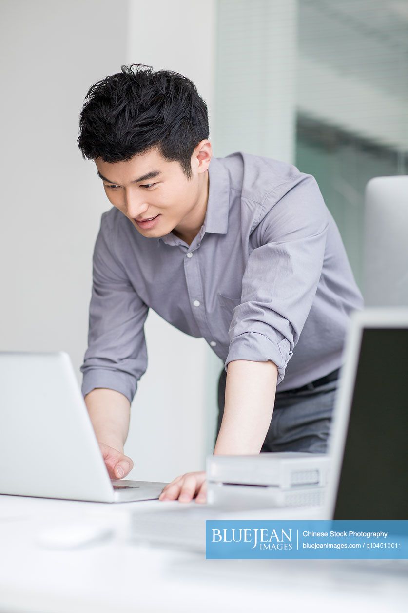 Young Chinese businessman using laptop in office