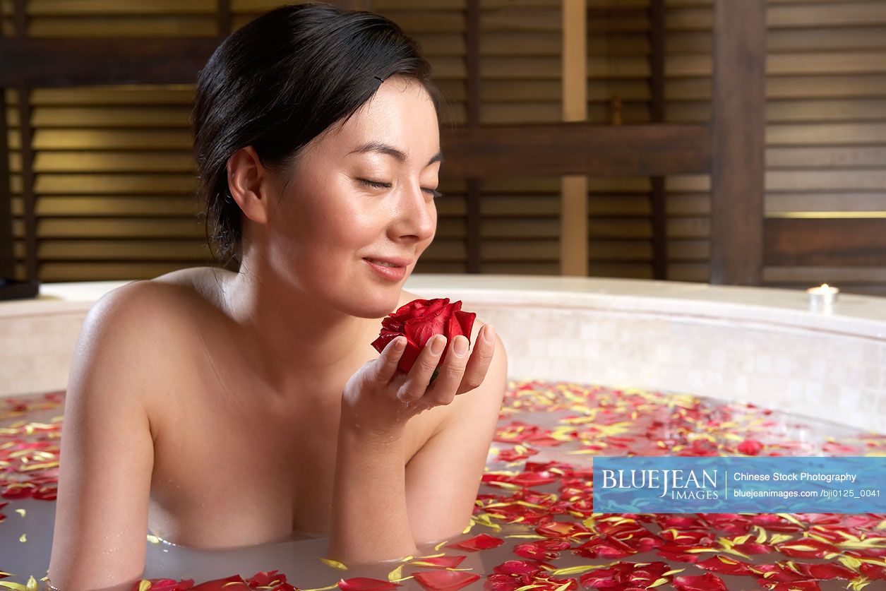 Chinese woman relaxing in a rose petal bath with an orchid and candle