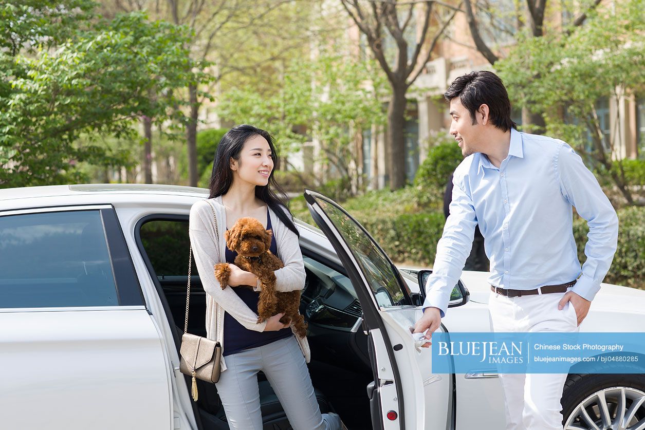 Young Chinese couple getting out of car with their pet dog