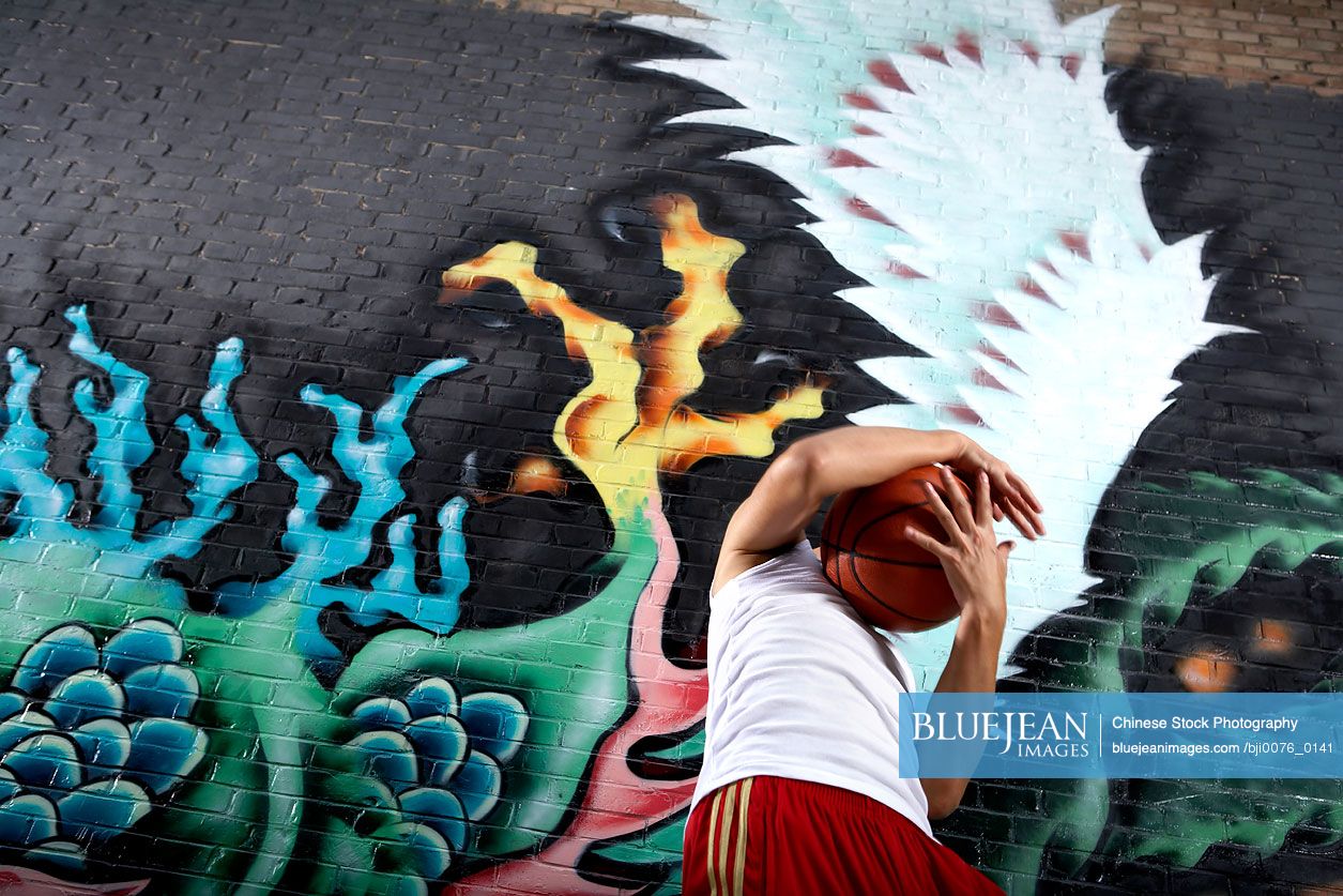 Chinese teenage boy with obscured face standing next to spray painted mural