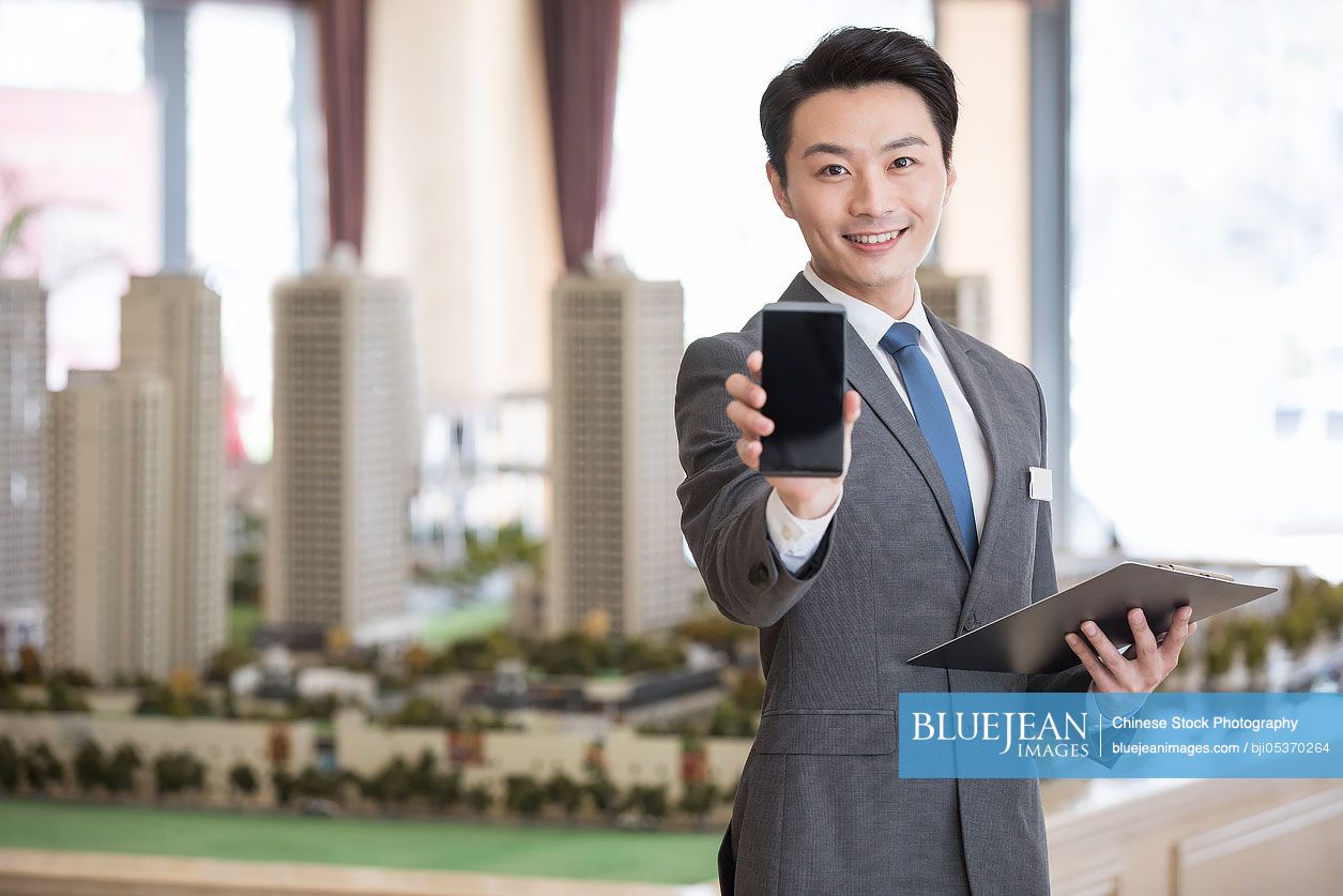 Confident Chinese realtor showing a smart phone