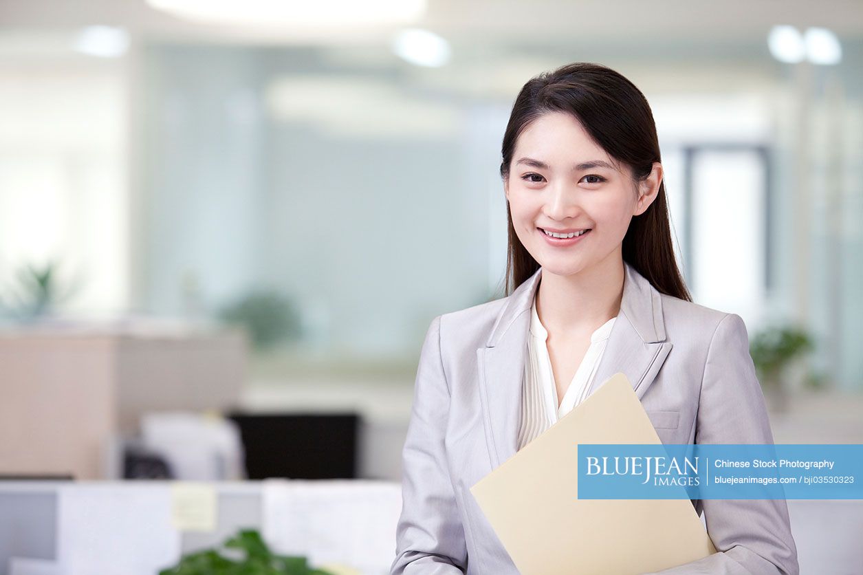 Cheerful Chinese office lady with a file in office