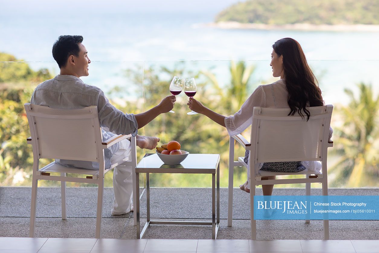 Happy young Chinese couple drinking wine on balcony