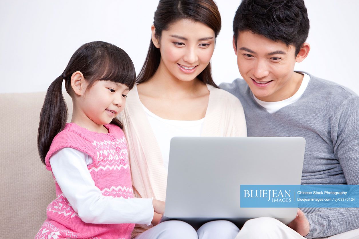 Happy young Chinese family sitting in sofa and sharing a laptop