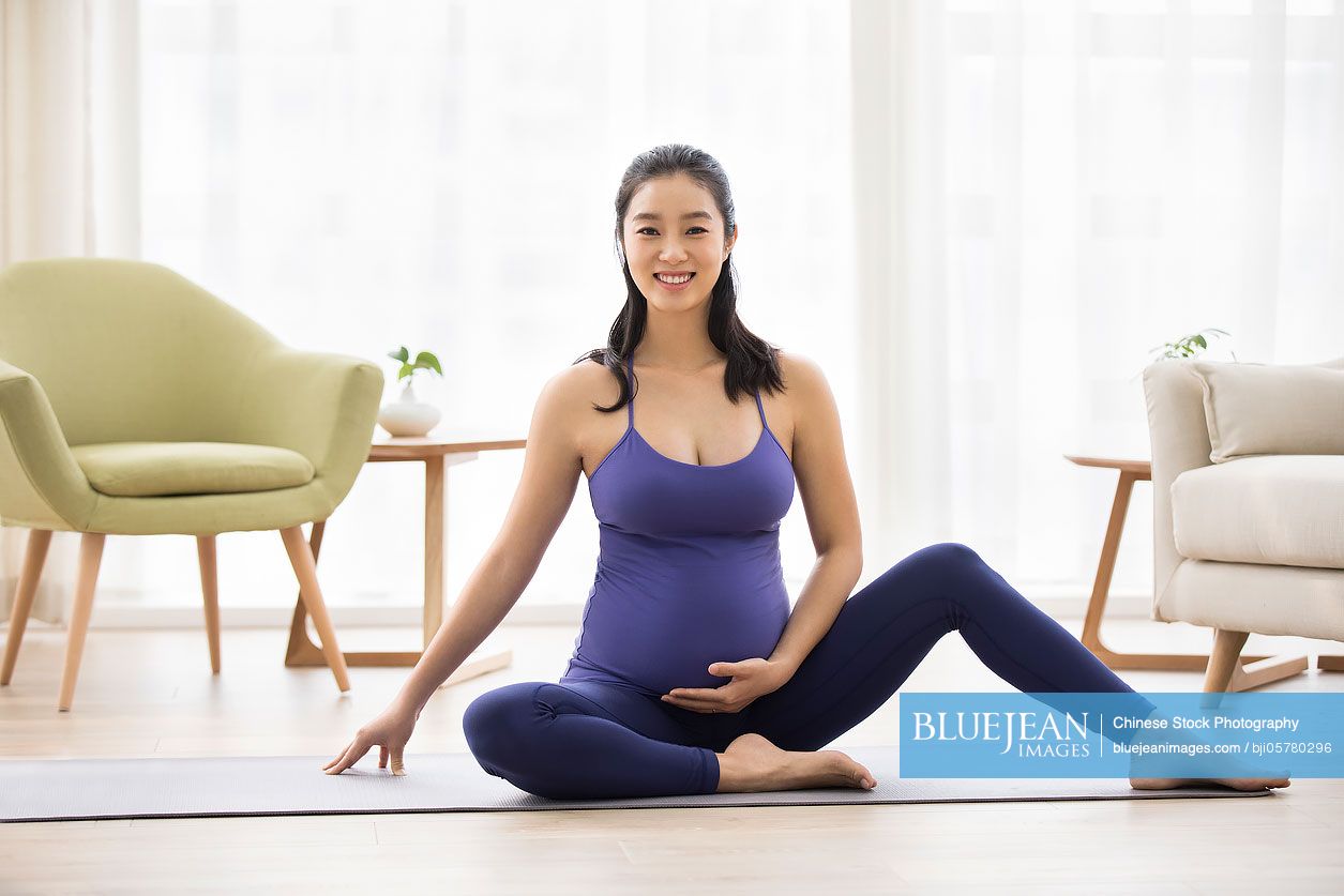 Cheerful Chinese pregnant woman practicing yoga at home