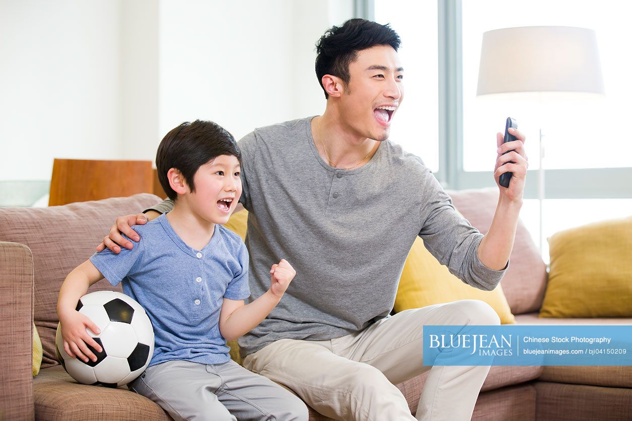 Excited Chinese father and son watching football on TV