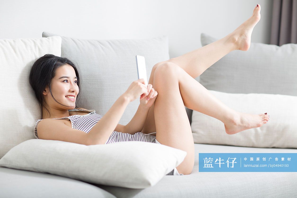 年轻女子躺在沙发上玩手机