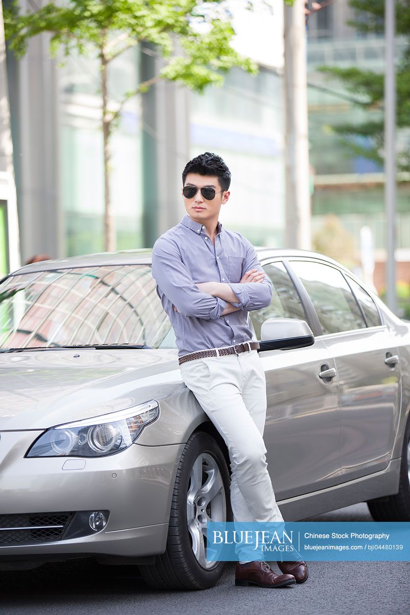 Young Chinese man leaning against his car