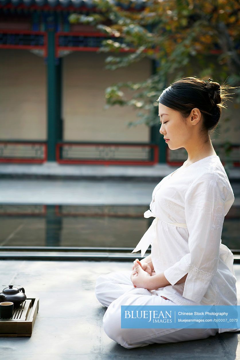 Chinese Woman Meditating Outdoors Next To Tea Set