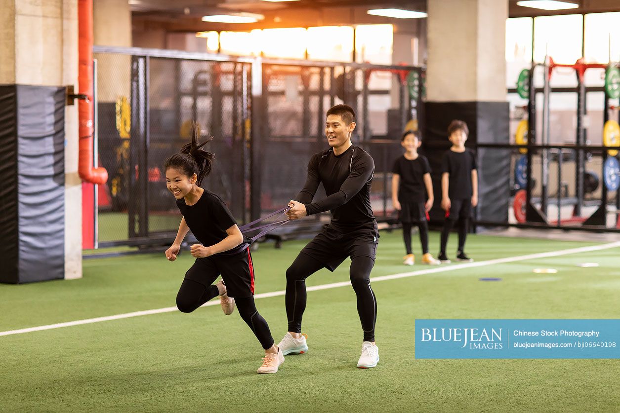 Active Chinese children having exercise class with their coach in gym