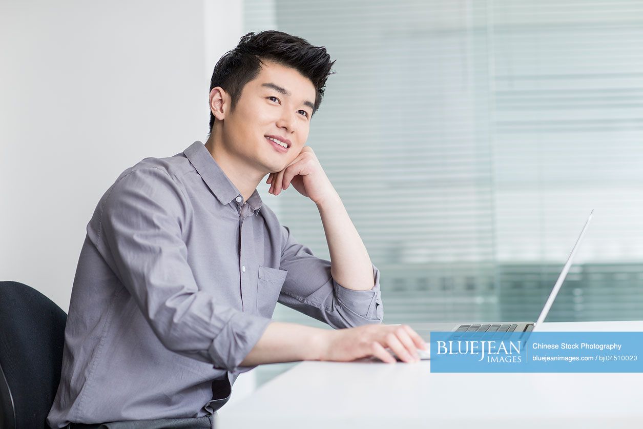 Young Chinese businessman using laptop in office