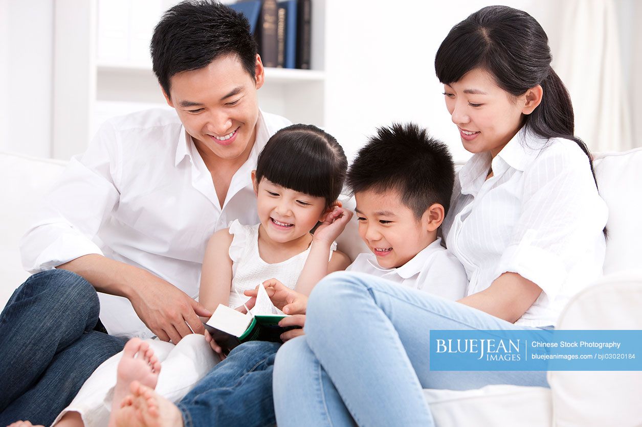 Happy Chinese family reading book in sofa