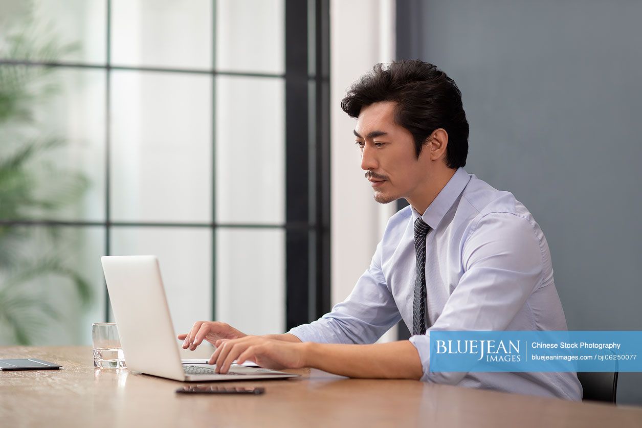 Successful Chinese businessman using laptop in office