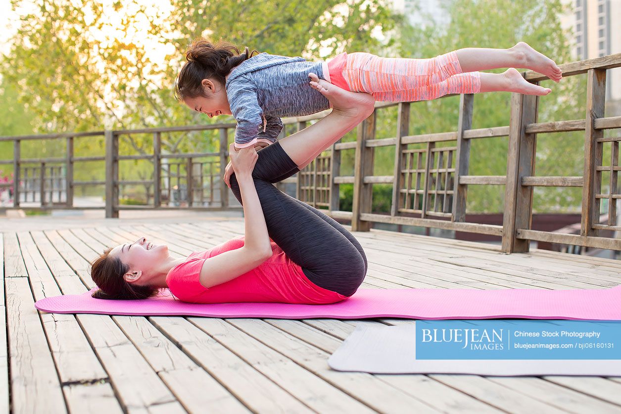 Happy Chinese mother and daughter doing yoga outdoors