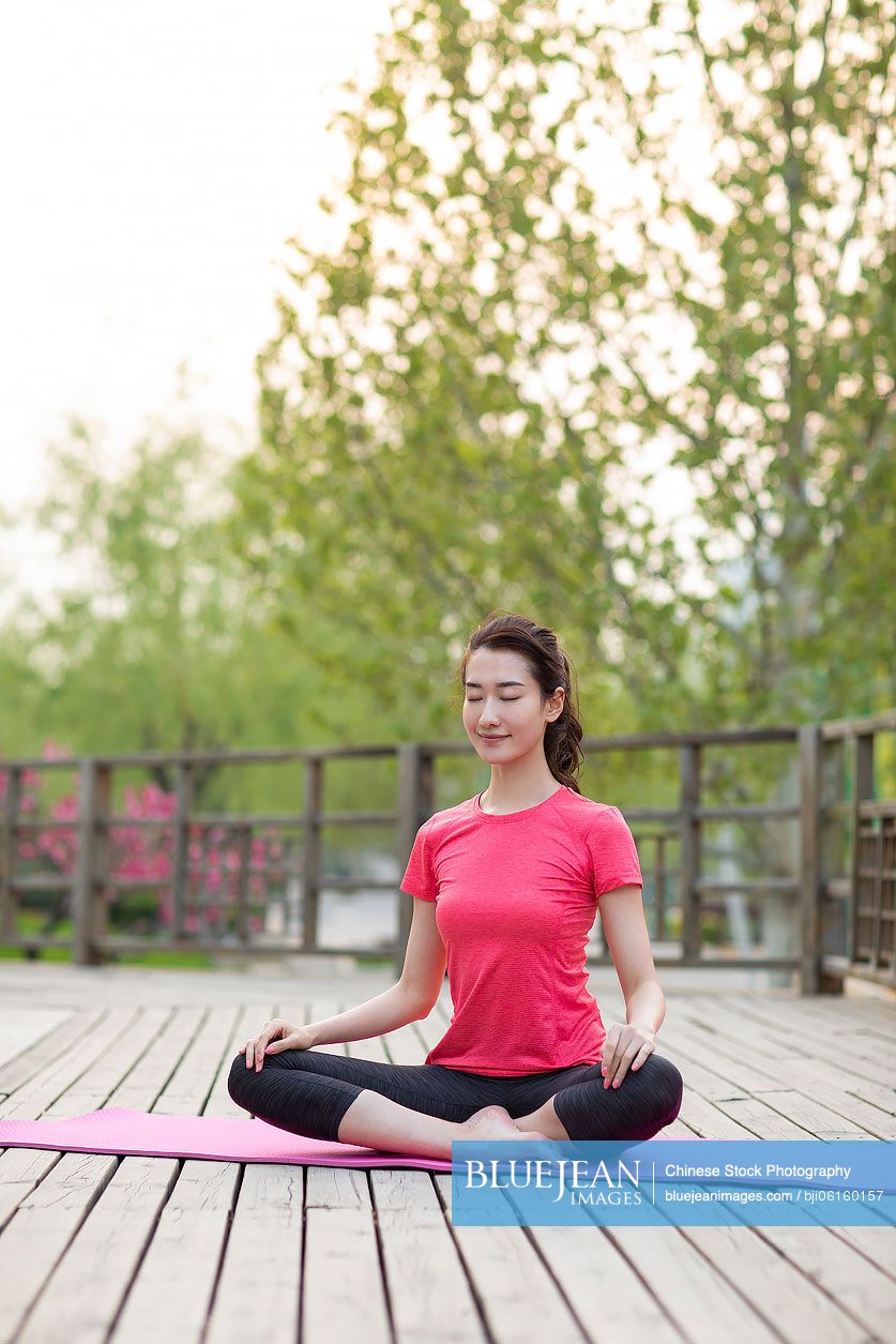 Happy young Chinese woman doing yoga in park