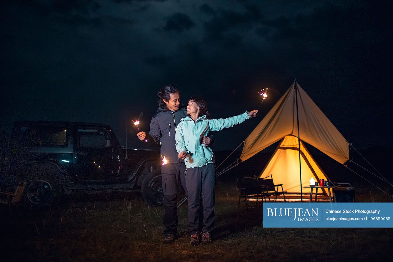 Happy Chinese couple holding sparklers and camping outdoors