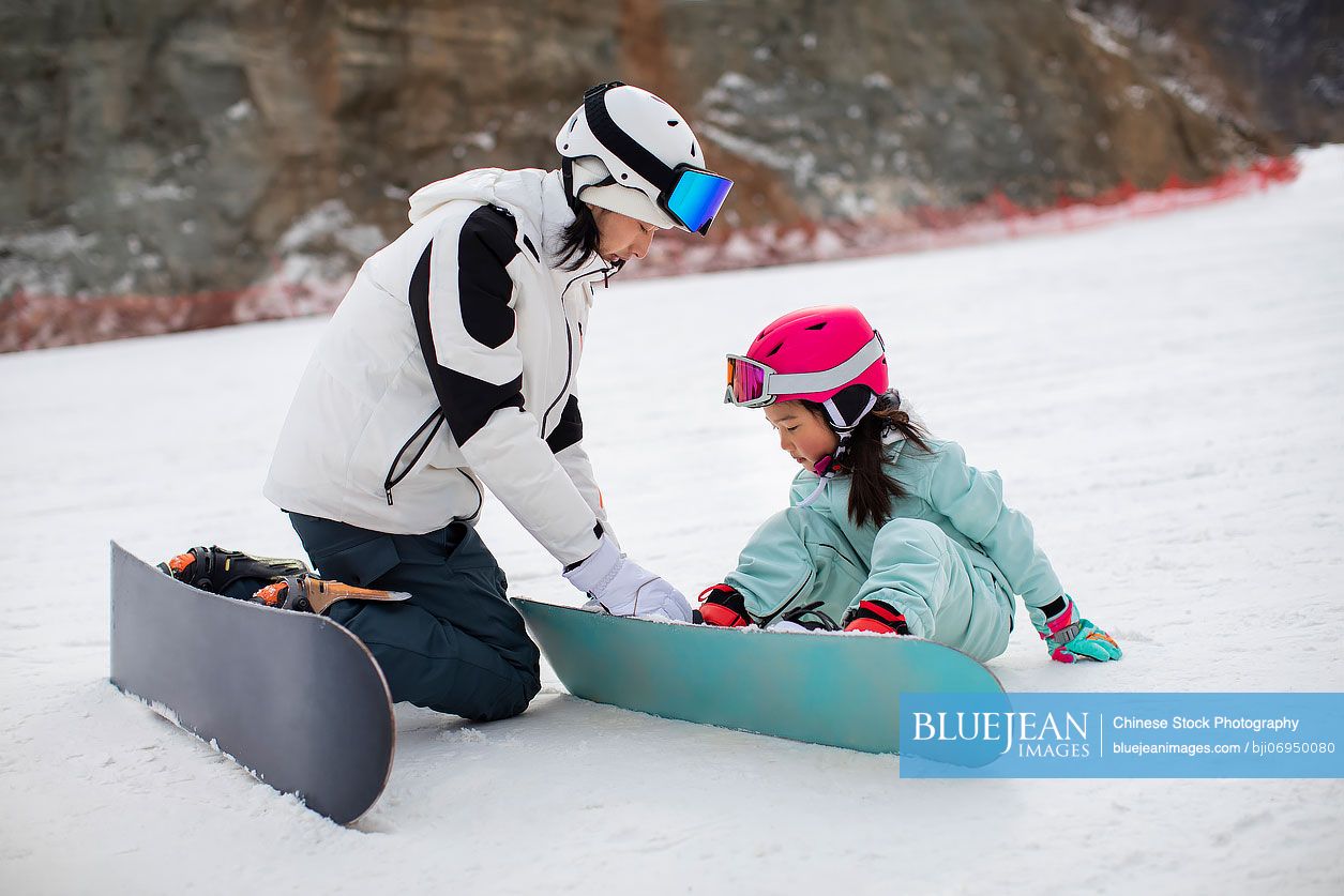 Little Chinese girl learning how to snowboard with her coach