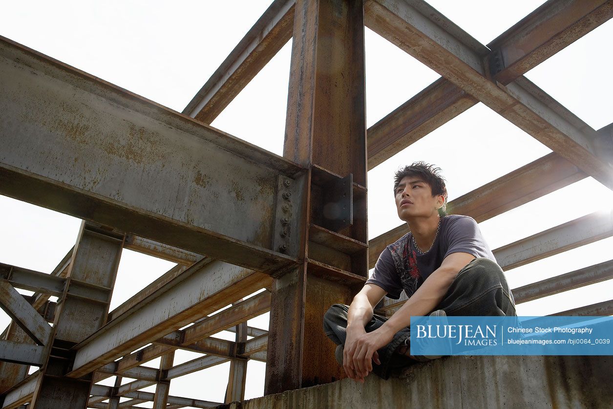Young Chinese man sitting on a beam in a construction site