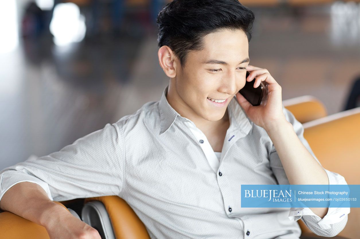 Young Chinese man talking on the phone in airport lounge