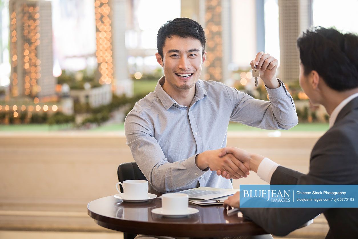 Happy young Chinese man buying new house from realtor