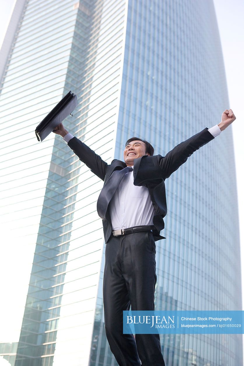 Chinese businessman jumping in front of tall building