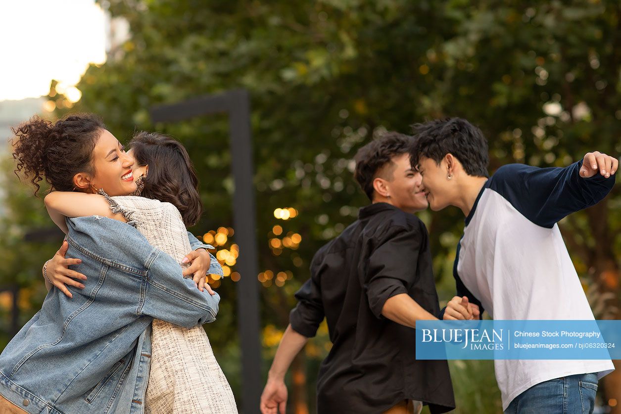 Fashionable young friends greeting and hugging on street