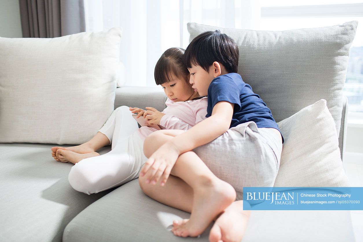 Happy Chinese boy and girl playing smart phone in sofa
