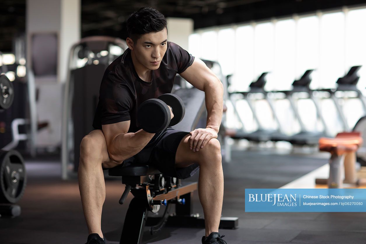 Young Chinese man working out with dumbbell at gym