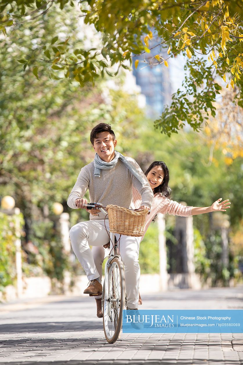 Happy young Chinese couple riding bike together on street