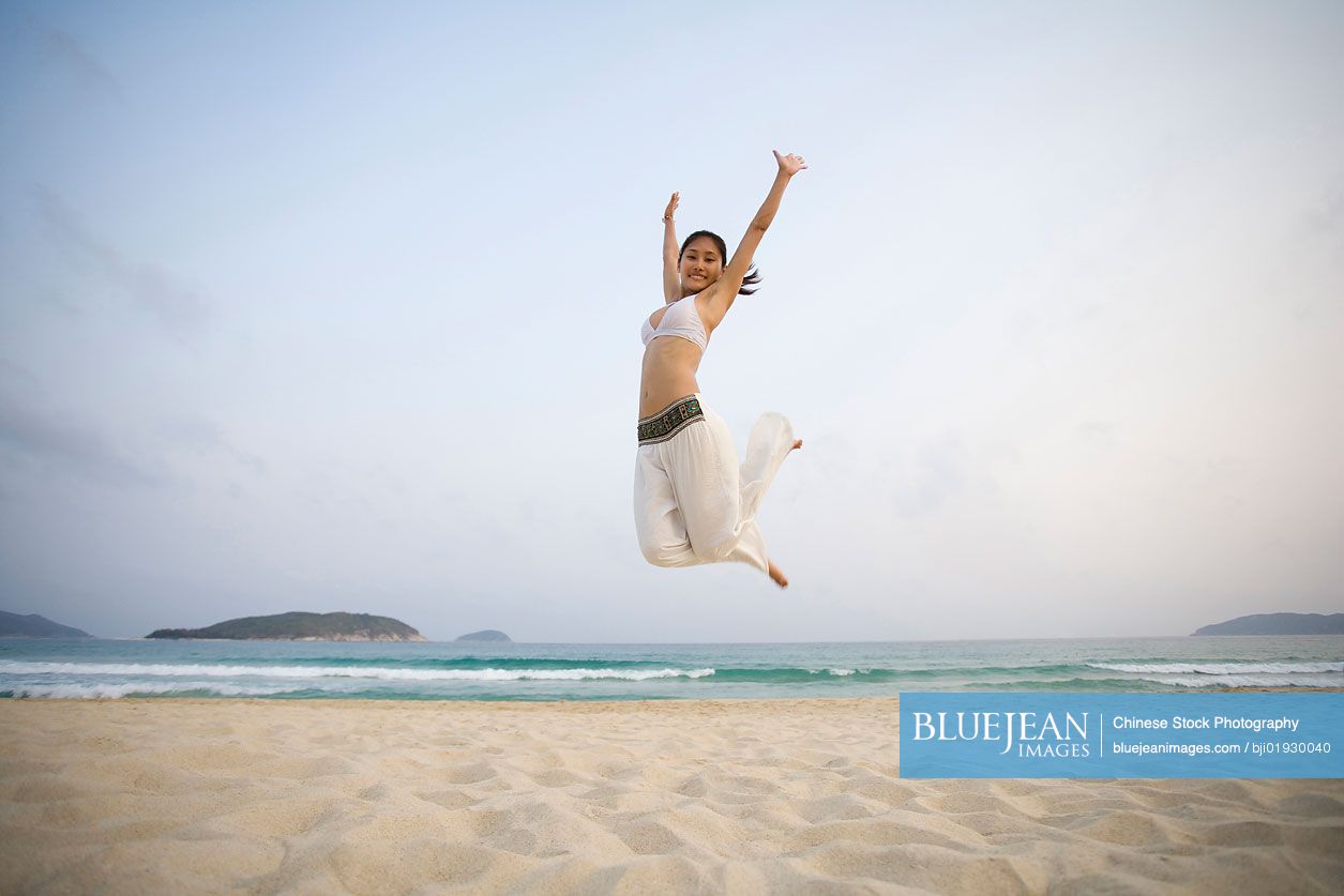 Young Chinese woman jumping on the beach
