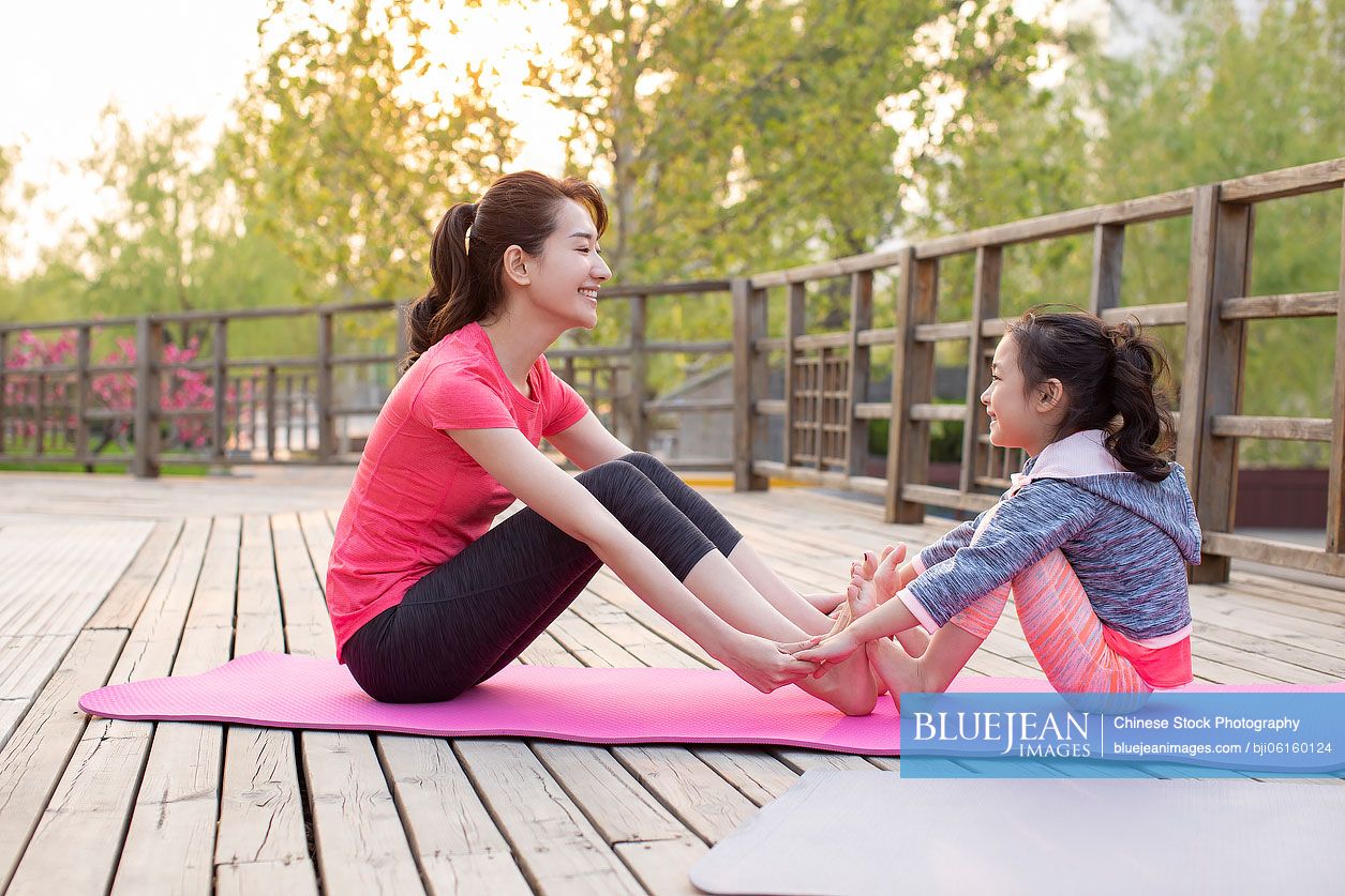 Happy Chinese mother and daughter doing yoga outdoors
