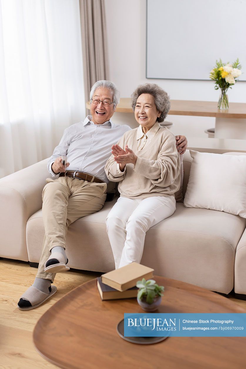 Cheerful senior Chinese couple watching TV at home