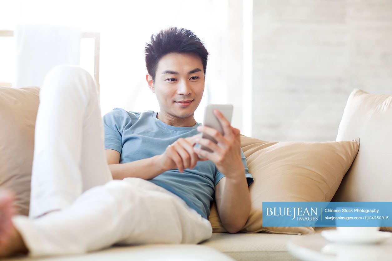 Young Chinese man using smart phone on the sofa