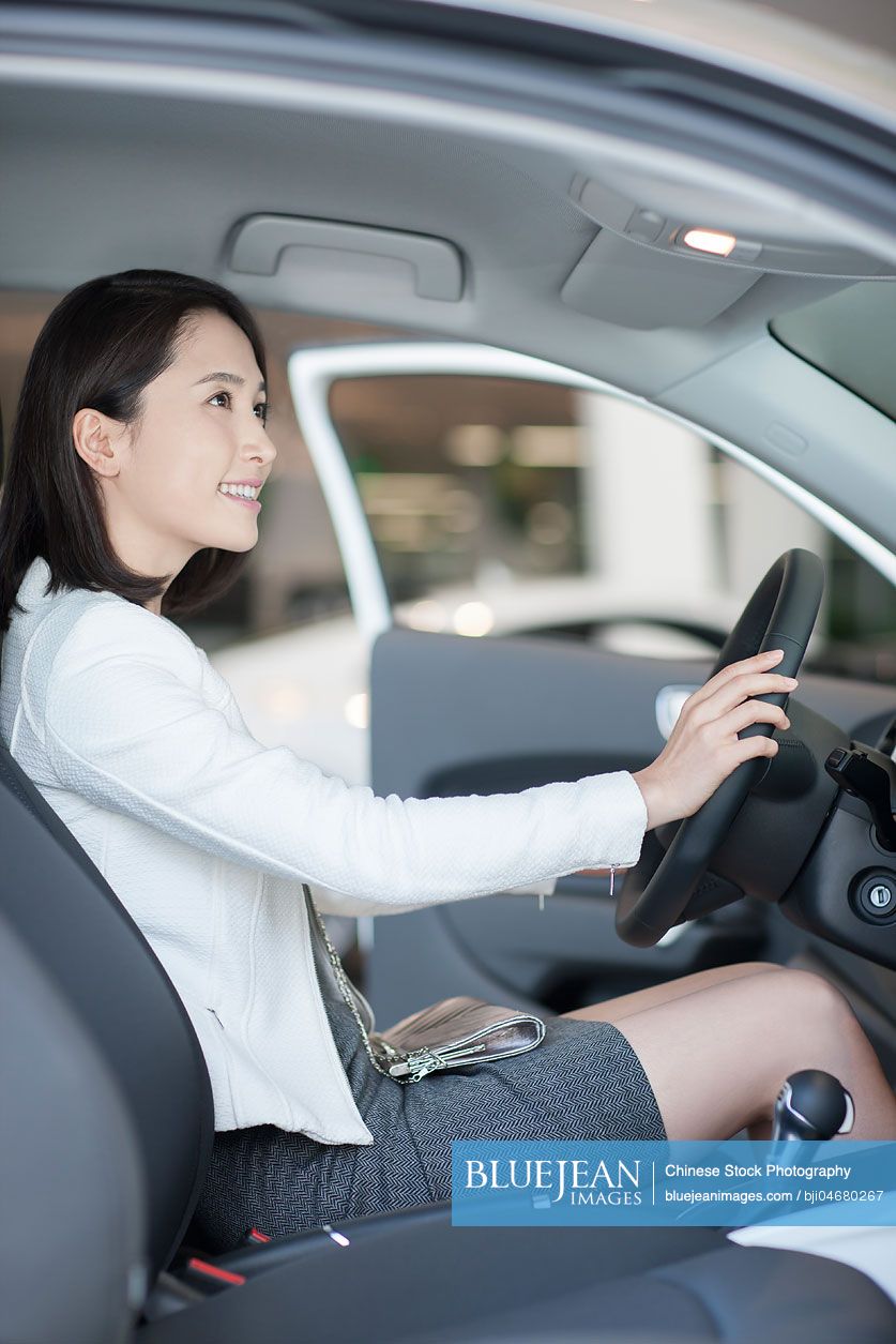 Young Chinese woman choosing car in showroom