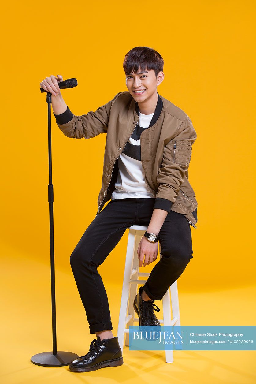 Cheerful young Chinese man singing with microphone