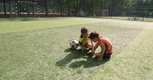 小女孩在足球场帮小男孩系鞋带