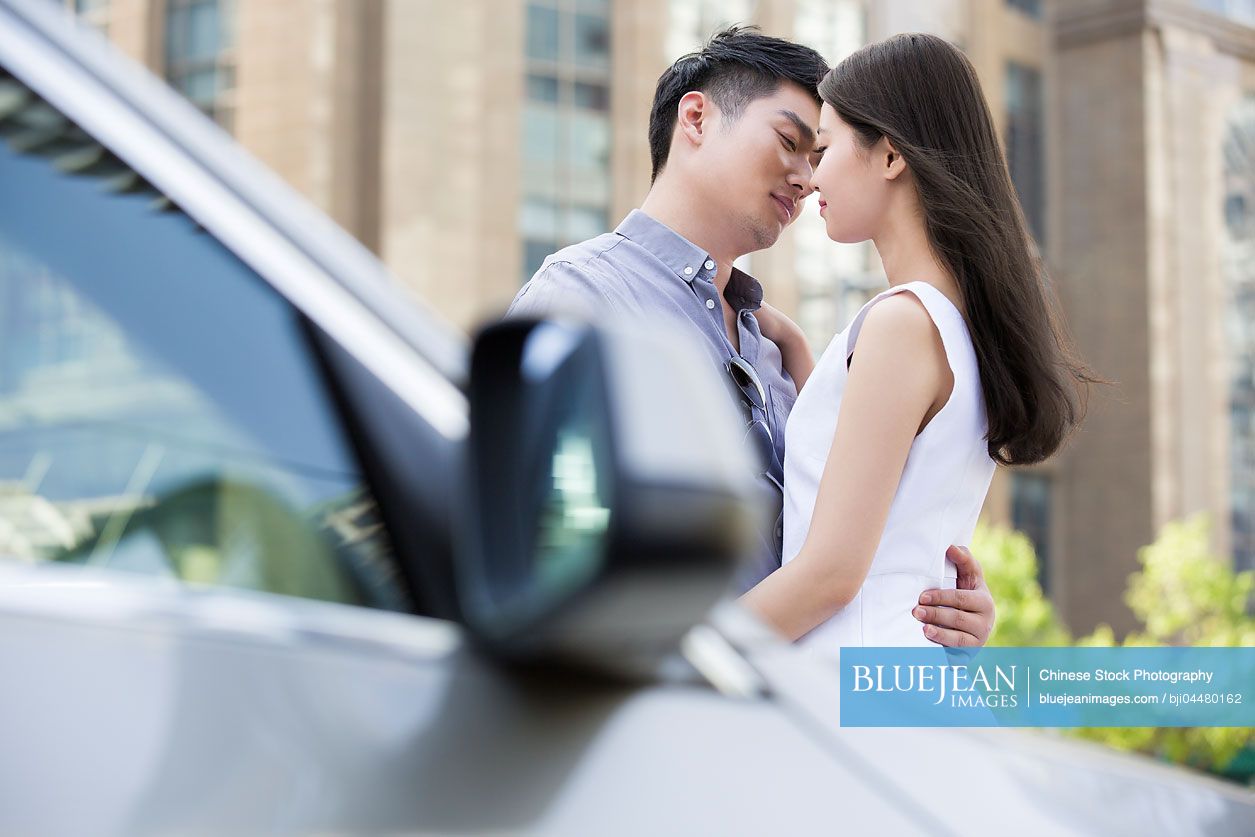 Young Chinese couple kissing next to their car