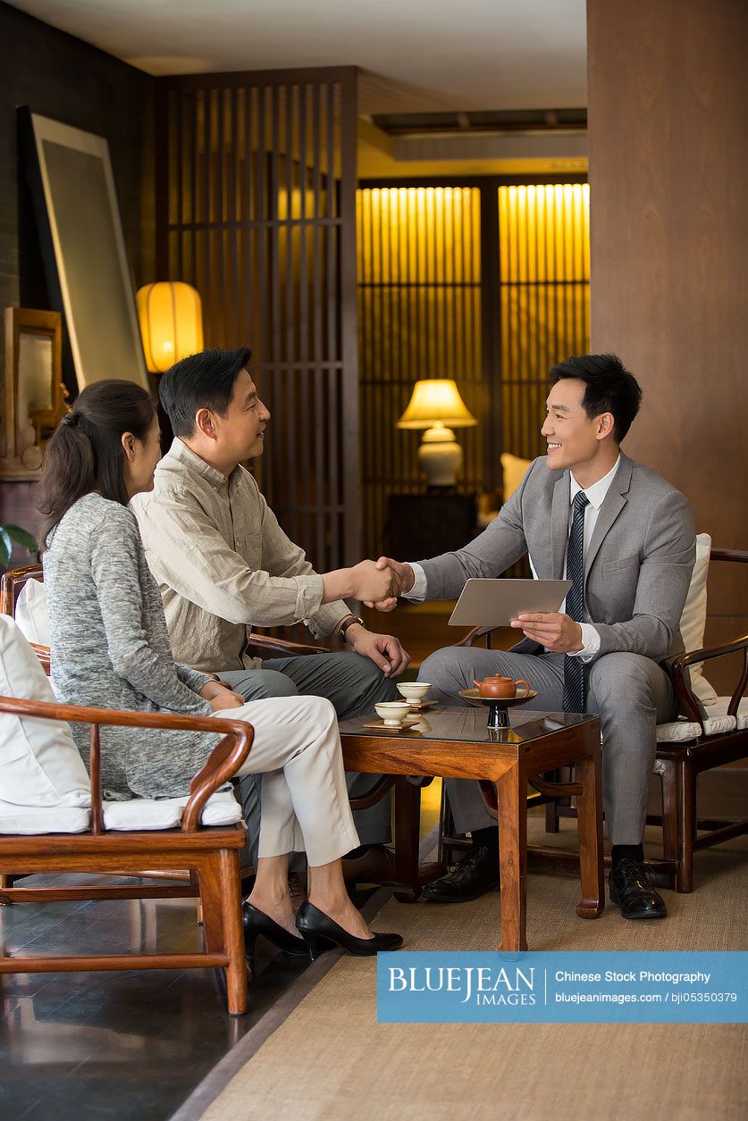Confident Chinese financial consultant shaking hands with mature couple