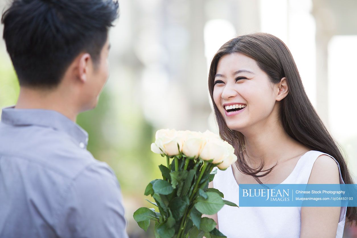 Young Chinese man giving flowers to girlfriend