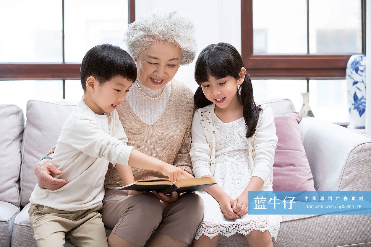 开心的奶奶和孙子孙女在沙发上看书