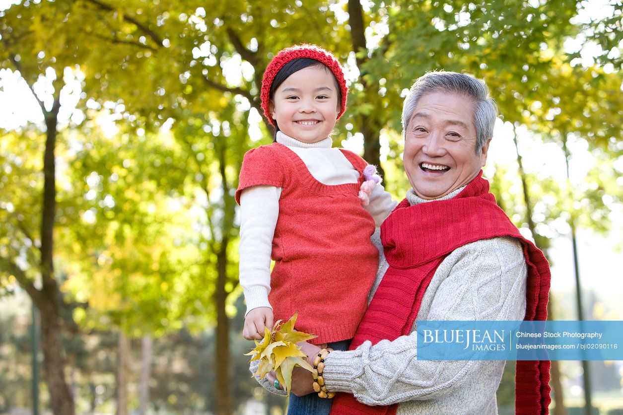 chinese-grandfather-holding-granddaughter-with-maple-leaves-in-hand