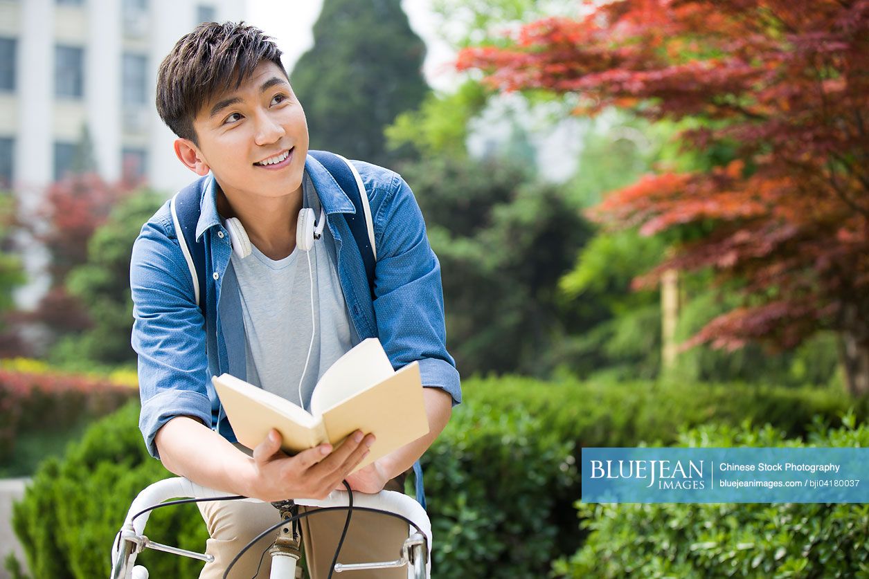 Male Chinese college student Reading on bicycle