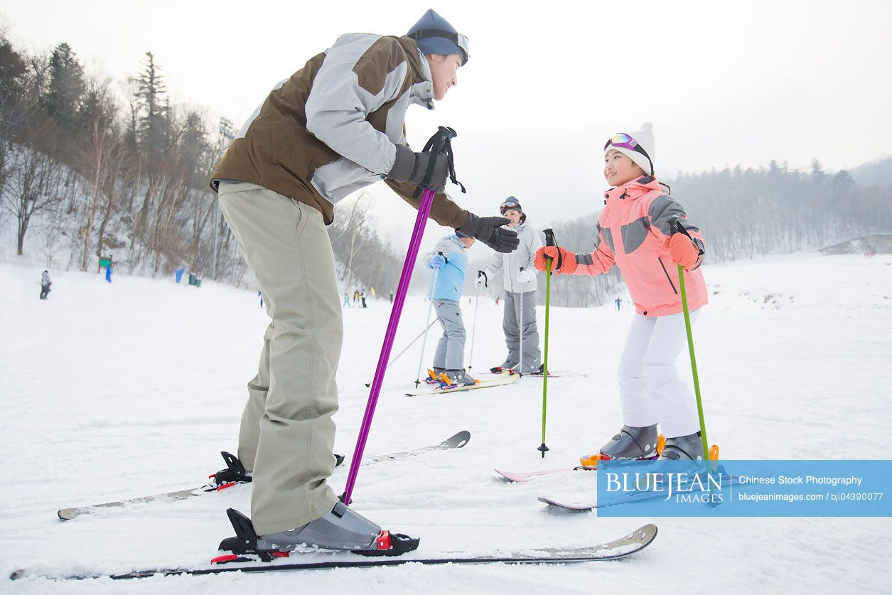 Young Chinese parents teaching children to ski