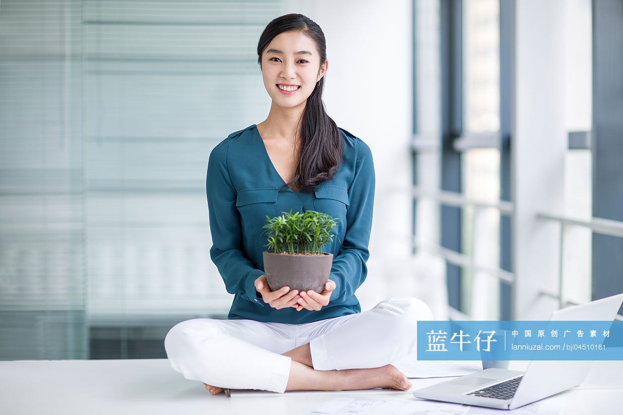 年轻商务女士抱着盆栽植物坐在办公桌上