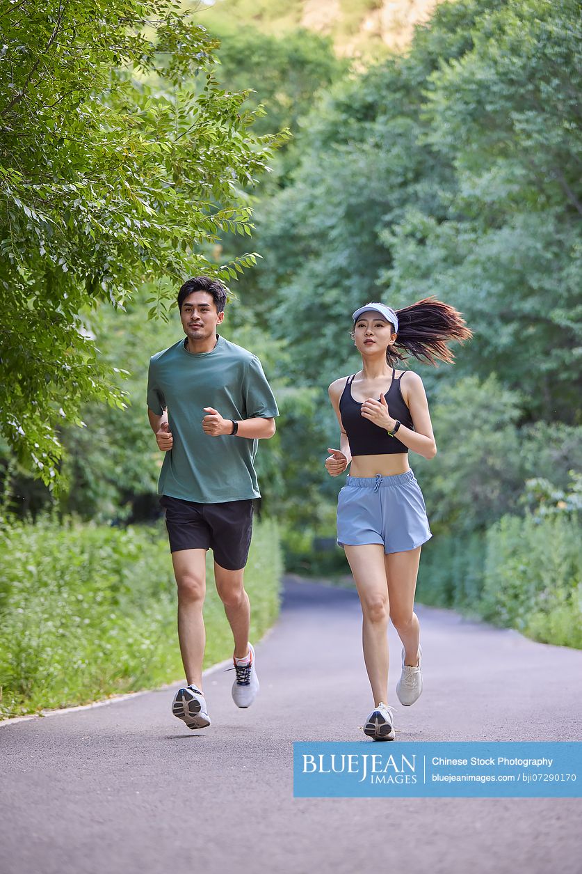 Young couple jogging along a road surrounded by lush trees