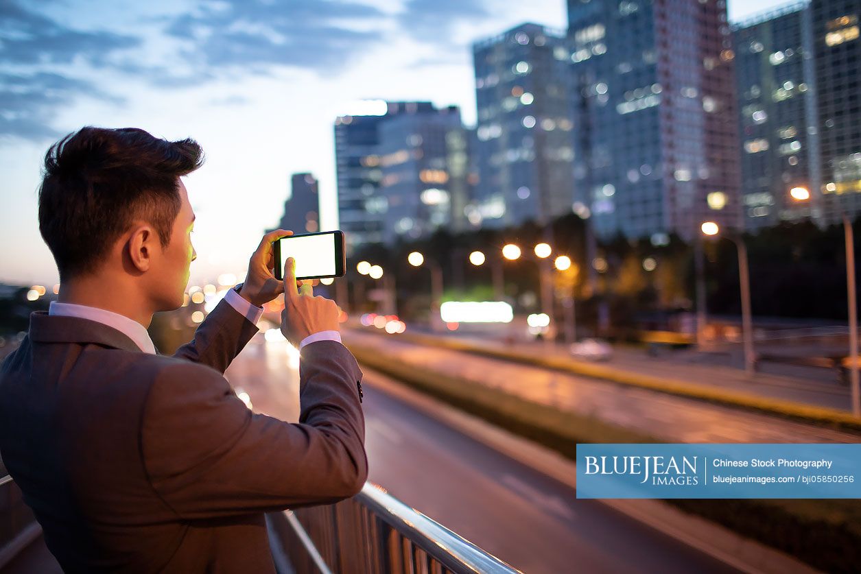 Young Chinese businessman taking photos with smart phone