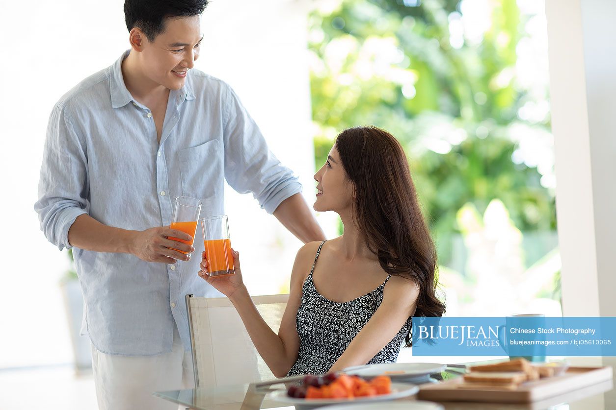 Happy young Chinese couple drinking juice in hotel room